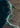 Aerial view of a winding turquoise river cutting through dark brown and black sedimentary terrain, creating branching channels and patterns of light and shadow.